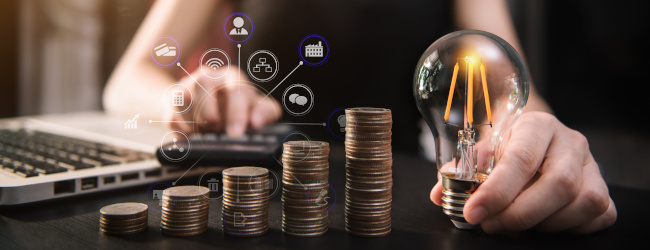 Abbildung: Energiepreispauschale - Geschäftsfrau Hand hält Glühbirne mit Laptop-Computer und Geldstapel im Büro.