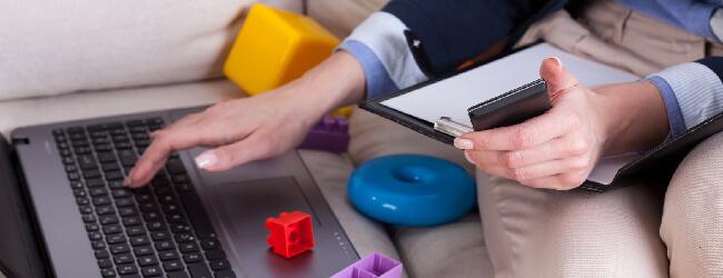 Abbildung: Frau arbeitet an Laptop zwischen Kinderspielzeug