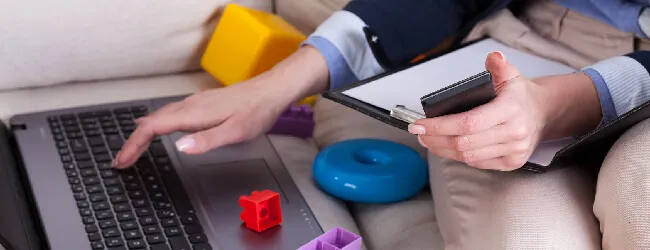 Abbildung: Frau arbeitet an Laptop zwischen Kinderspielzeug